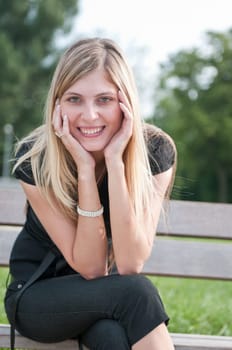 Portrait of young beautiful smiling woman siting on bench in park outside