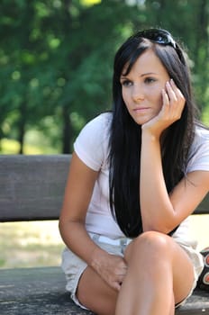Young sad and pensive woman siting on bench in park - detail