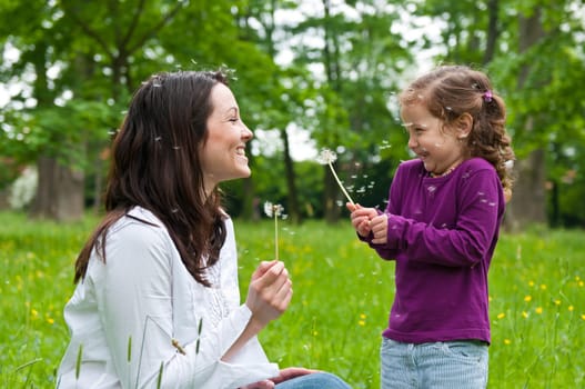 Mother with small daughter blowing to dandelion - lifestyle outdoors scene in park
