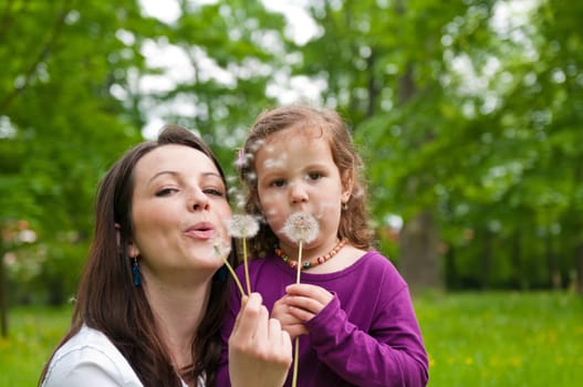 Mother with small daughter blowing to dandelion - lifestyle outdoors scene in park