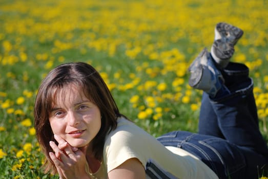 Young woman lying in field of dandelions with blurred background