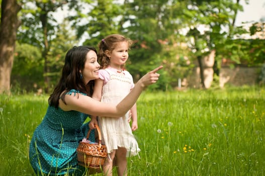 Mother shows with finger to her cute little daughter something interesting in distance