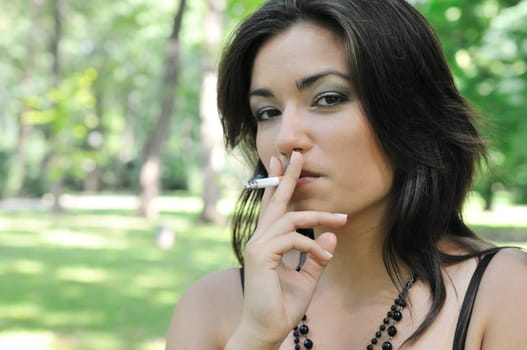 Portrait of young woman smoking cigarette outdoors in sunny green park