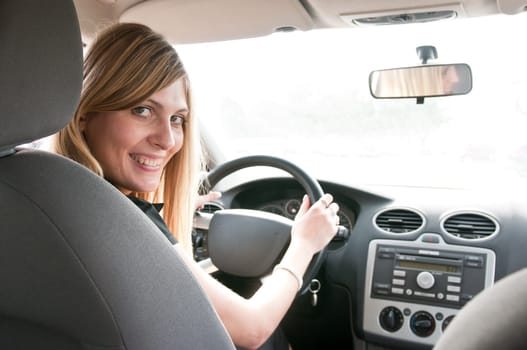 Portrait of young smiling woman siting behind steering wheel inside car