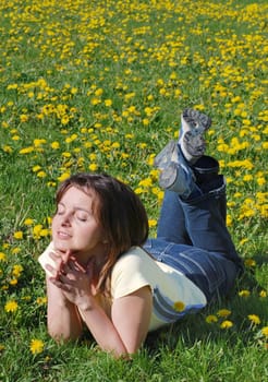 Woman lying in field of dandelions with face turned to sun