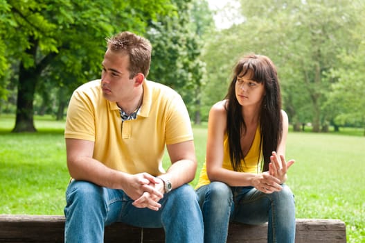 Young couple sitting outdoors on bench having relationship problems