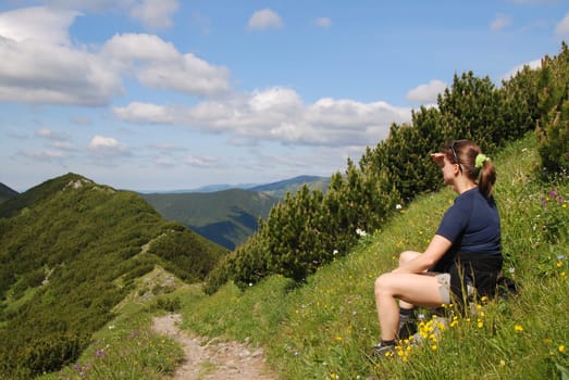 Hiking woman siting in grass and looks to mountains