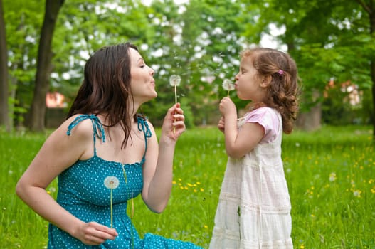 Mother with small daughter blowing to dandelion - lifestyle outdoors scene in park