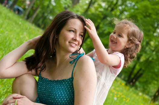 Cute girl is playing with mother&#039 s hair - outdoors scene