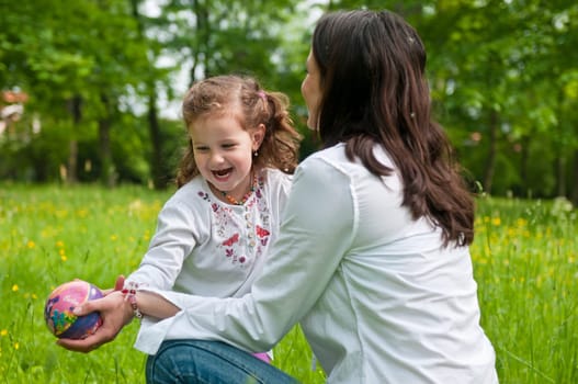 Small cute girl enjoying lifetime with her mother outdoors in park - plying with ball