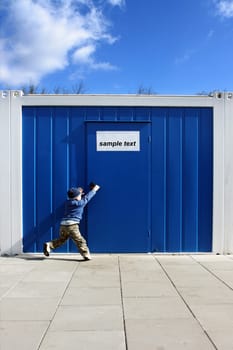 Baby boy wants to open the door handle near blue cellular homes.