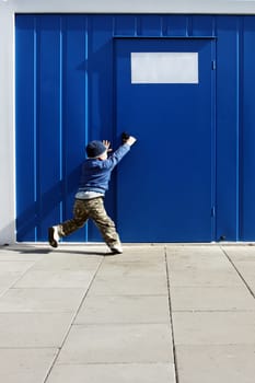 Baby boy wants to open the door handle near blue cellular homes.