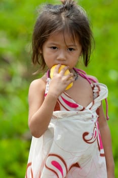 Portrait of girl from Asia,child in poor clothes eating mango