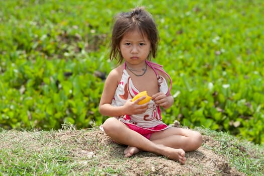 Portrait of girl from Asia,child in poor clothes eating mango