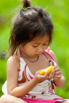 Portrait of girl from Asia,child in poor clothes eating mango