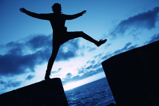 Silhouette of a woman jumping into the air on a wall, against blue cloudy sky. Concept for happiness and activity.