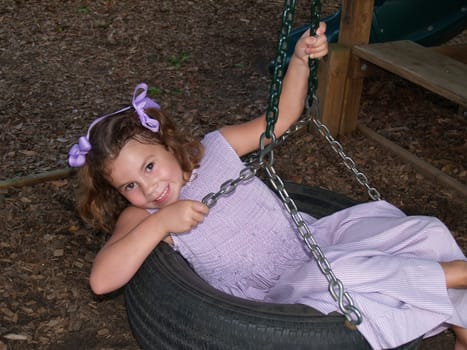 Young girl smiling and swinging on a tire swing.