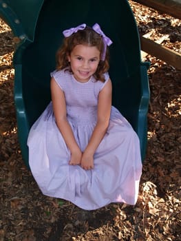 Young Girl Sitting at the end of a green tube slide on a playground.
