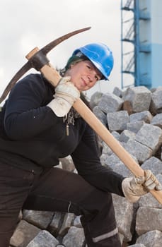 Female blue collar worker in protective clothes holding pickaxe