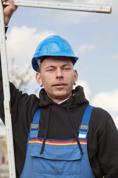 Manual worker in hard hat stands outdoor with foldable ruler