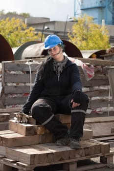 Female manual worker in blue hard hat seating on wooden palette outdoor