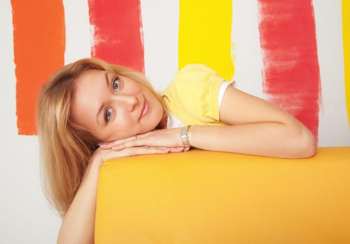 Portrait of pretty young woman lean on a yellow leather sofa