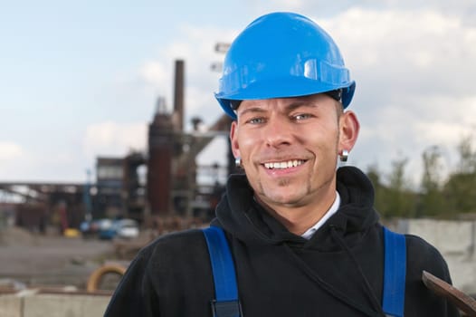 Smiling worker in blue hard hat standing against industrial background
