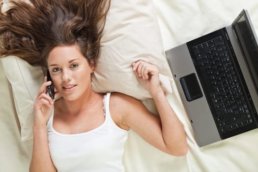 Undressed young woman lying in bed and talking on cellphone
