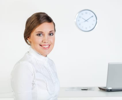 Young pretty smiling businesswoman standing in front of her desk in the office