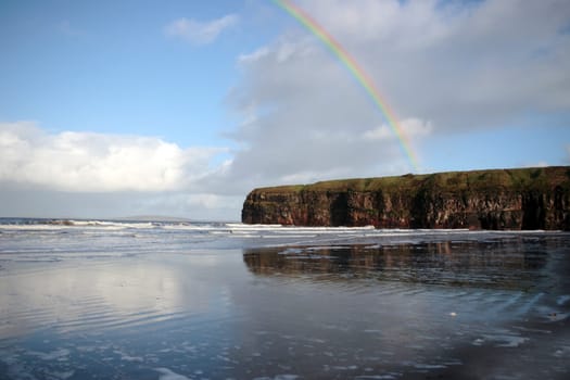 a view of the beach cliffs in ballybunion co kerry ireland with rainbow reflection on a wet stormy day