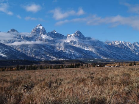 Teton mountains in Wyoming with snow and low clouds behind a homestead farm in Grand Teton National Park.