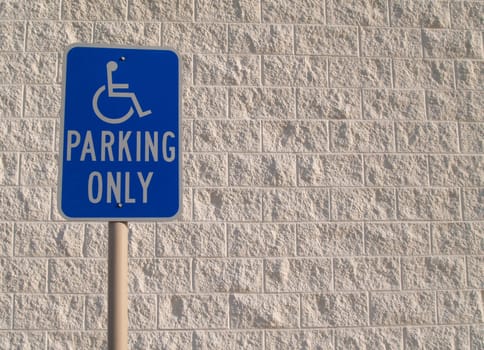 Blue handicap parking sign with a white textured concrete block background that can be used for copy space.