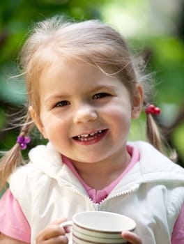 Little girl standing outdoors with milk cup and has a milk beard