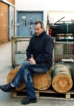 Businessman sitting next to his red bank company outdoors looking depressed.