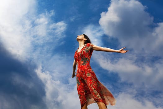 Pretty young woman with arms raised standing almost weightlessly towards the sun