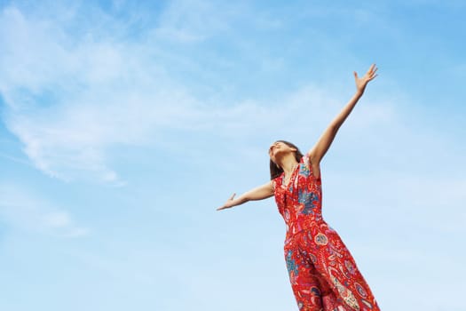 Pretty young woman with arms raised standing on blue sky