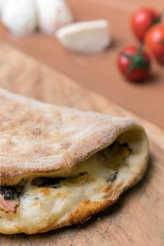 Italian food, closed calzone pizza on rustic wooden background. On blurred background small red tomatoes and white mozzarella.
Selective focus