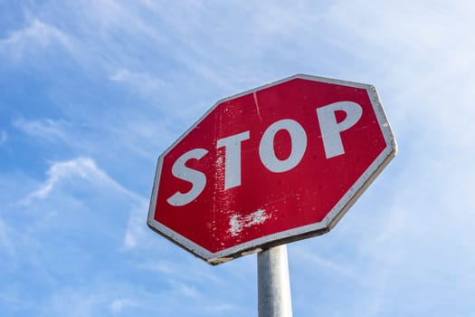 Stop road sign on a blue sky background with white clouds.