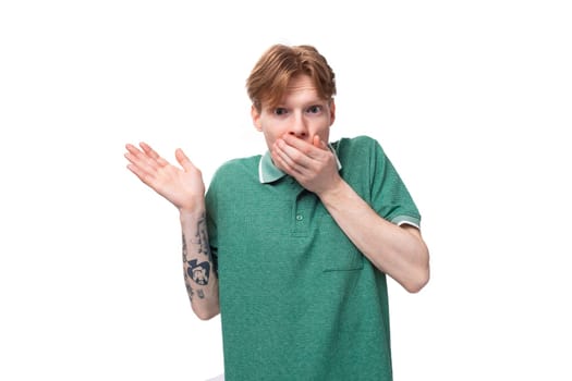 young surprised ginger man with a tattoo on his arm dressed in a green short sleeve t-shirt is shocked.