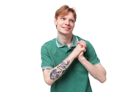 young charming adorable ginger man with a tattoo on his arm dressed in a green short sleeve t-shirt against the background with copy space.