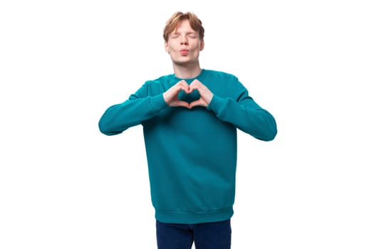 young caucasian student guy with red hair in a blue sweater shows a heart.