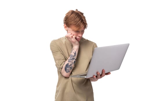 young red-haired man with glasses dressed in a brown shirt uses a laptop for study.