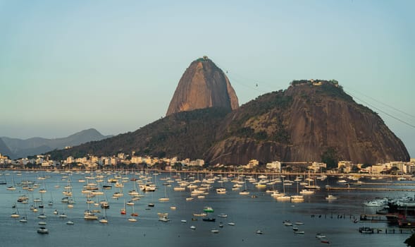 Iconic dusk scene of Sugarloaf Mountain & Morro da Urca with sailboats at Botafogo Bay in Rio de Janeiro, ideal for travel and tourism.