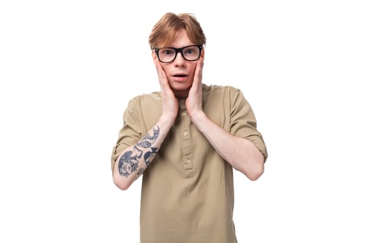 young handsome man with copper hair with a tattoo on his arm is wearing a brown shirt.