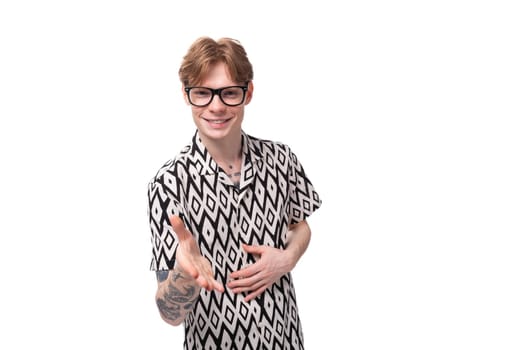 a young man with red hair in glasses and a summer black and white shirt extends his hand in greeting.
