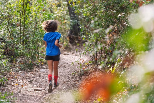 rear view of a kid practicing trail running in the forest, concept of sport for children in nature and healthy lifestyle, copy space for text