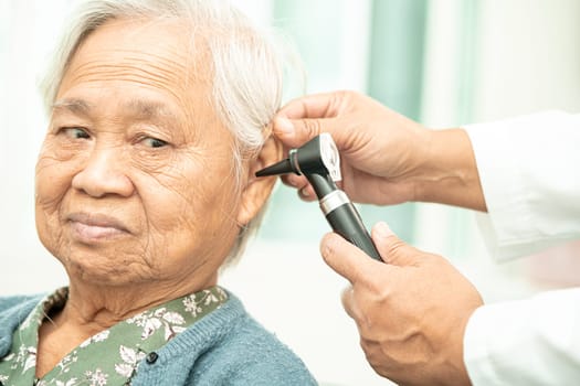 Audiologist or ENT doctor use otoscope checking ear of asian senior woman patient treating hearing loss problem.