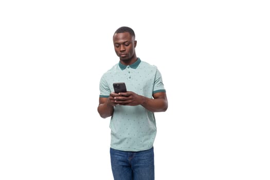 young cute american guy dressed in a mint t-shirt uses a smartphone for social networks.
