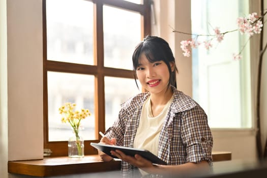 Portrait of beautiful Asian woman using digital tablet at table in cafe.