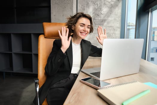 Young professional, woman connects to business meeting, online conference or chat, talking to laptop, gesturing while having conversation or giving speech.
